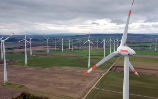 Foto des Windpark Dardesheim: Man sieht viele Windräder auf Feldern vor wolkenverhangenem Himmel.