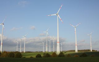 Foto des Windparks in Dassow, Windpark Schönberg. Mehrere Windräder auf Wiese mit Bäumen und blauem, leicht bewölktem Himmel.