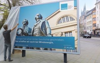 Man sieht einen Mann, der ein Plakat für mehr Windenergie in Thüringen enthüllt.