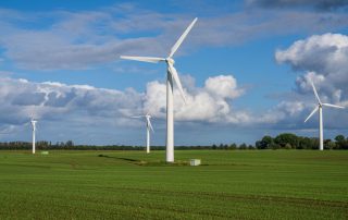 Man sieht vier Windräder auf grüner Wiese vor blauem Himmel mit Schäfchenwolken als Symbolbild für Windenergie als Wirtschaftsförderung
